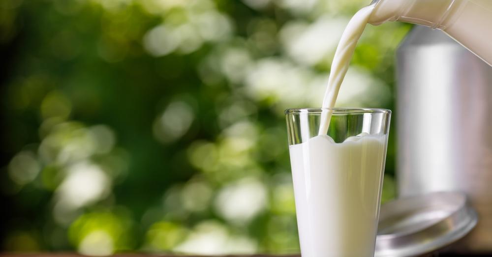 To the right of the frame, milk is being poured from a jug into a glass. The glass is on a wooden surface.