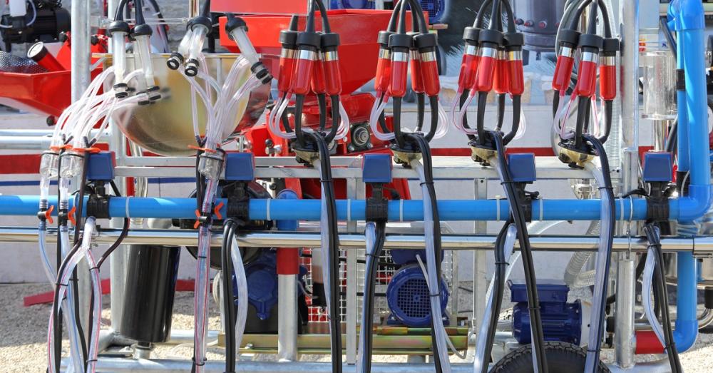 A large mobile milking machine with red and black cups in an outdoor facility with gravel underneath.