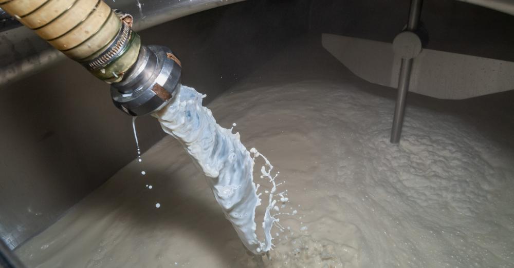 A yellow hose stretches down into a metal tank dumping fresh milk into the pool of curled substance below.