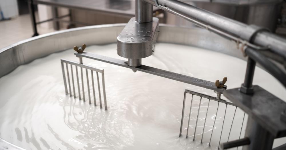 Mixers stirring the milk in a tank contained in a facility as ripples spread across the white surface.