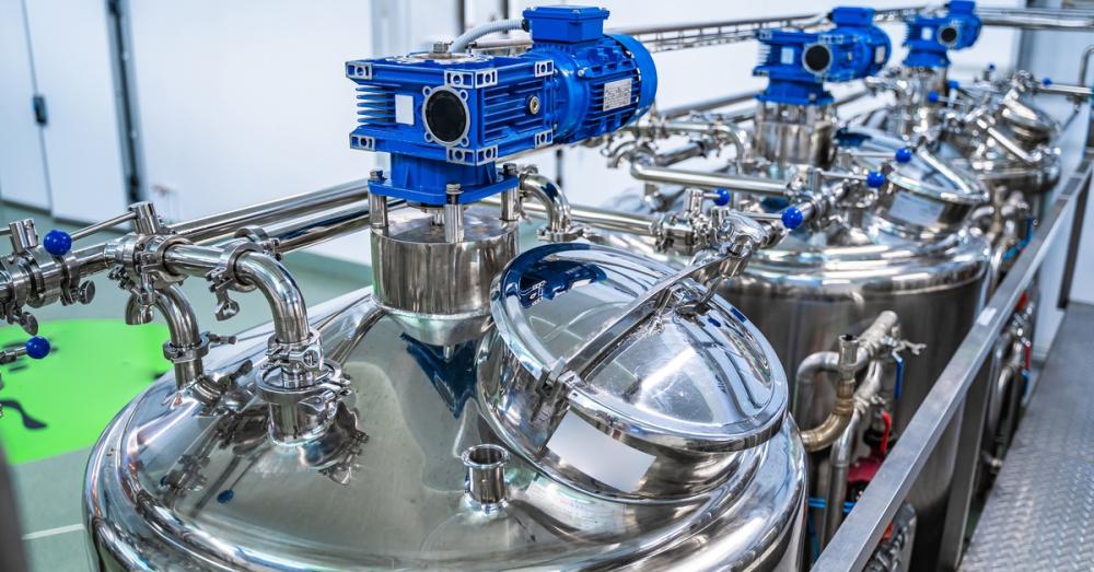 Multiple milk tanks lined up in a dairy facility, with clean exteriors and blue motors housed on top of each.