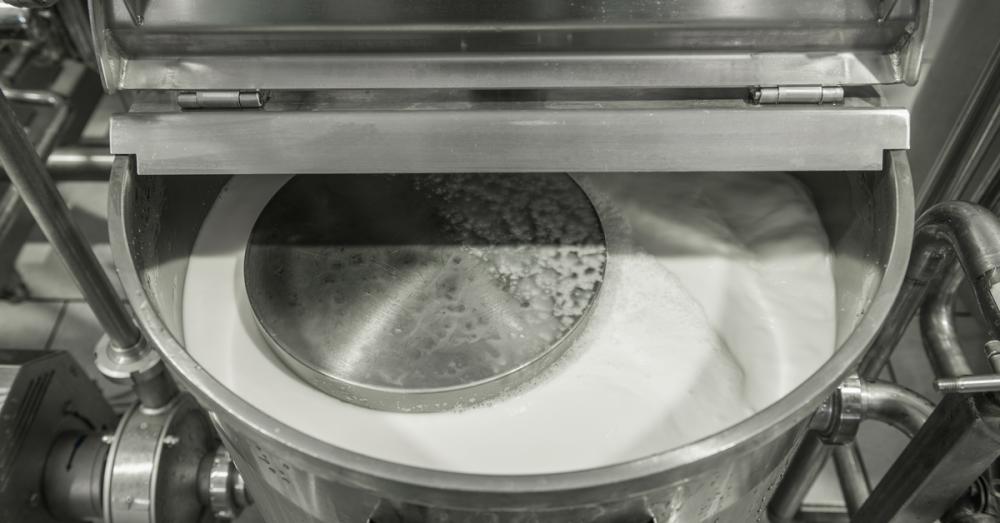 An open stainless-steel tank holds white liquid. A circular metal component sits partially submerged within the tank.