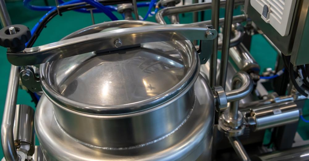 Close-up, downward view of the top of a closed, industrial metal tank. Opaque blue tubing feeds into the tank.