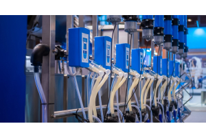 Multiple milking system components are arranged in a line, with blue control boxes and clear and opaque tubes.