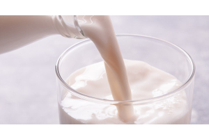 A close-up shot of a clear milk bottle pouring milk into a glass of milk against a white background.