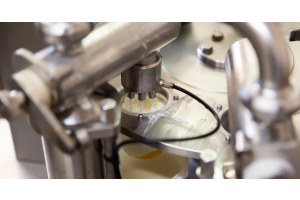 A milk processing machine expelling milk into the opening of a filled tanker as metal parts shine with cleanliness.