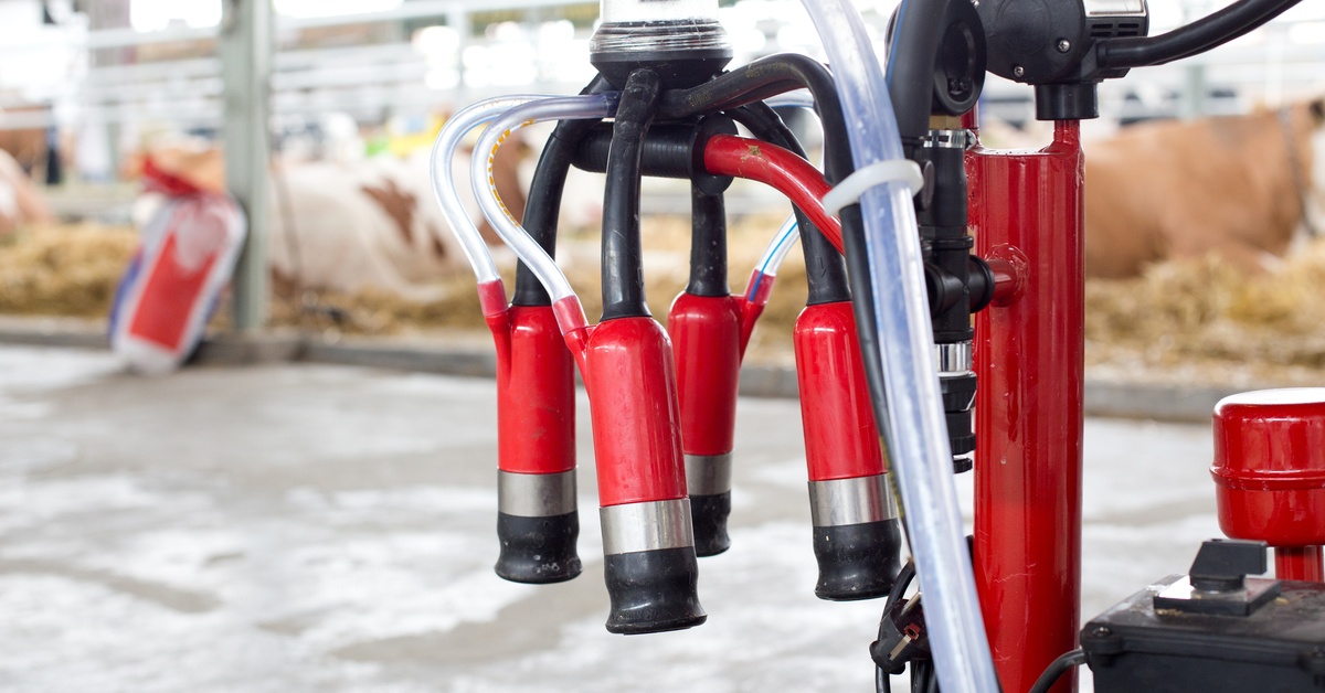 A portable milking machine with a red, black, and silver design in a barn with stables of cows in the background.