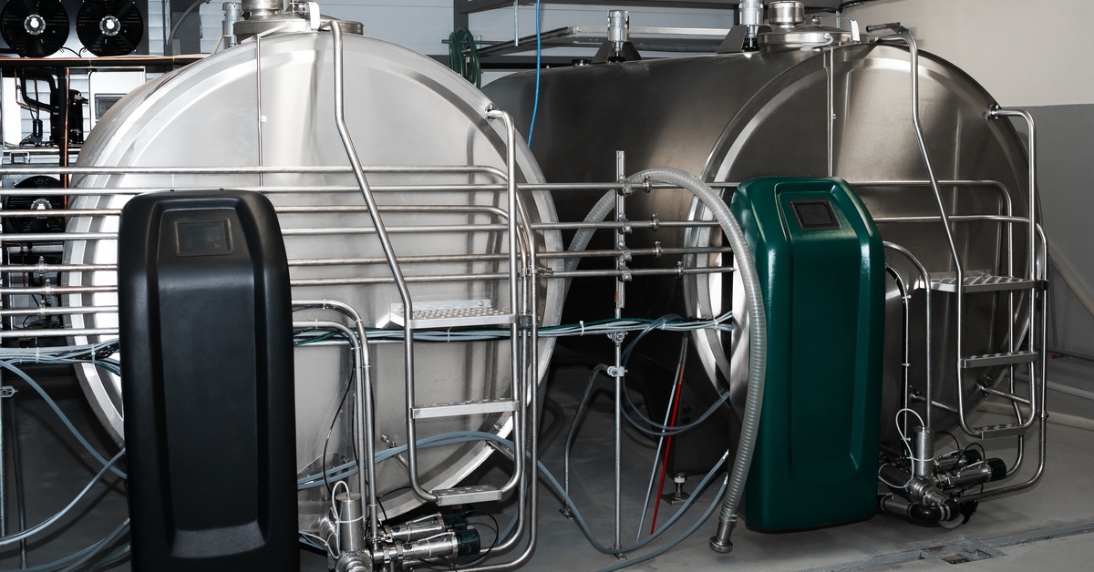 Two milk cooling tanks placed next to each other with a black and green terminal on the left and right, respectively.