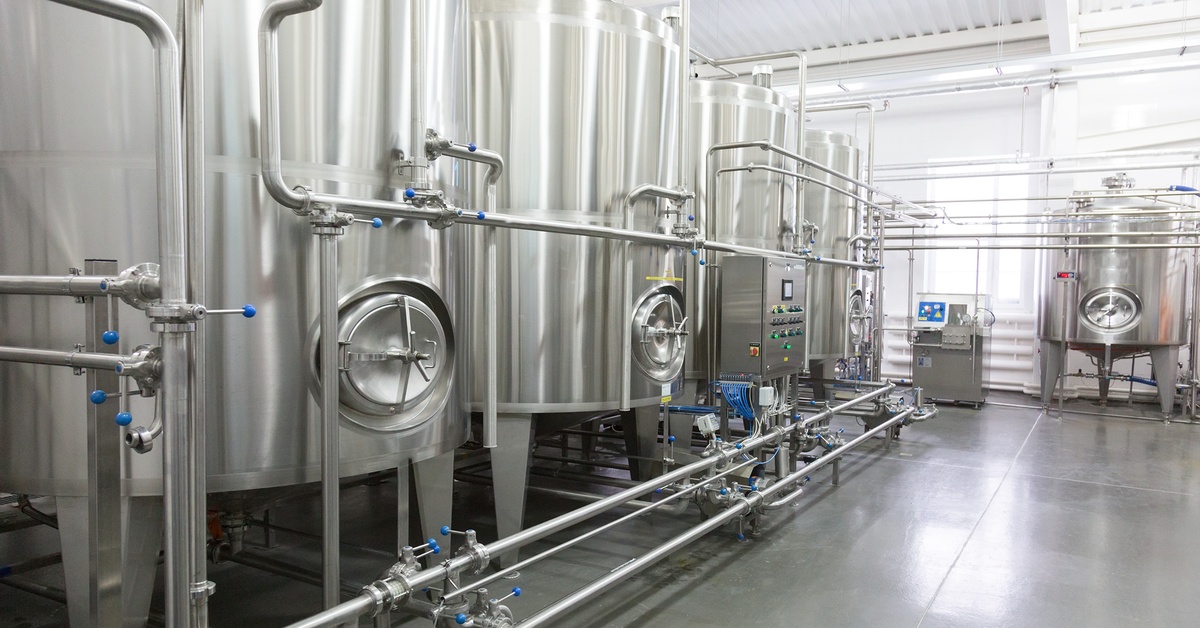A bright room contains several large stainless steel tanks with gauges. They are connected by metal pipes and valves.